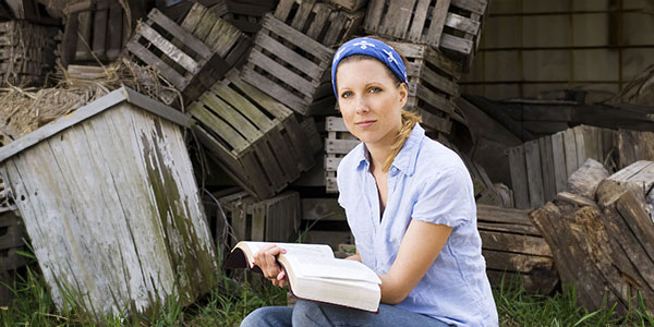 A missionary reading her bible while kneeling beside rundown housing materials and debris